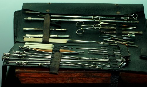 A collection of various metal surgical tools neatly arranged in a black case on a wooden surface.