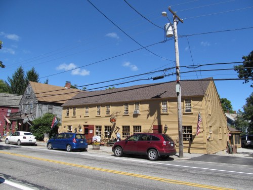 A yellow wooden building with multiple windows, parked cars in front, and a clear blue sky overhead.