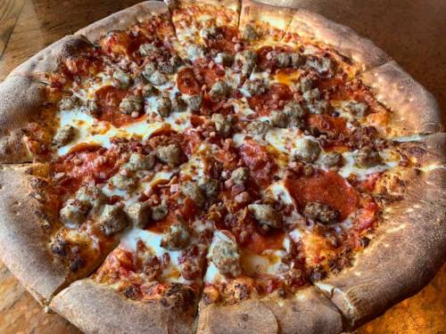 A large pizza topped with pepperoni, sausage, and bacon on a golden-brown crust.