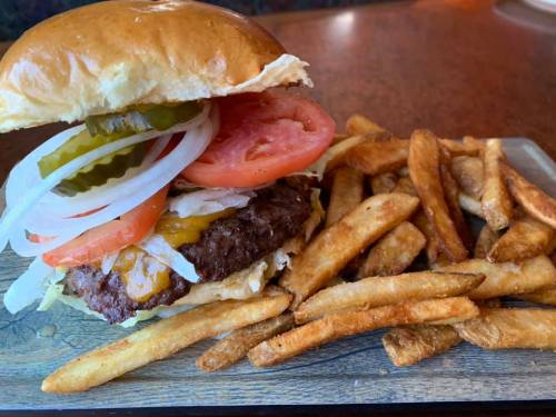 A juicy burger with lettuce, tomato, pickles, and onions, served with a side of crispy French fries on a wooden platter.