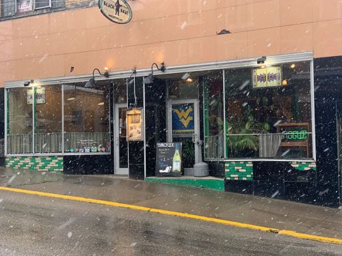 A storefront with large windows, featuring a West Virginia logo, during snowfall on a city street.