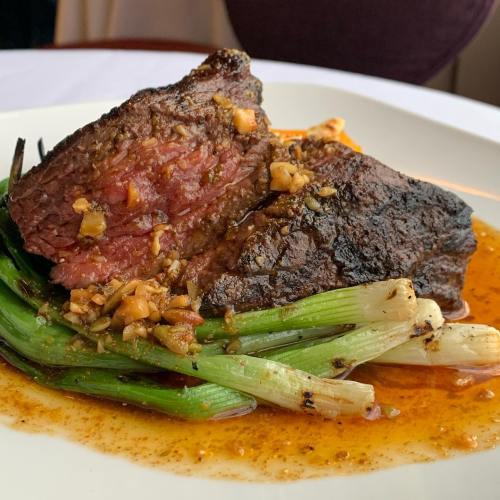 A succulent piece of beef, cooked medium-rare, garnished with garlic and served on a bed of grilled green onions.
