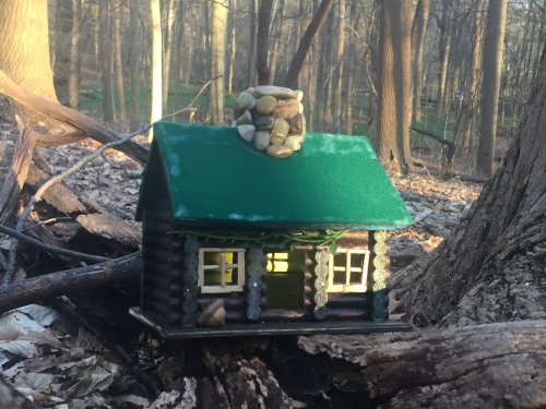 A small, whimsical cabin made of wood and stones, nestled among trees in a forest setting.