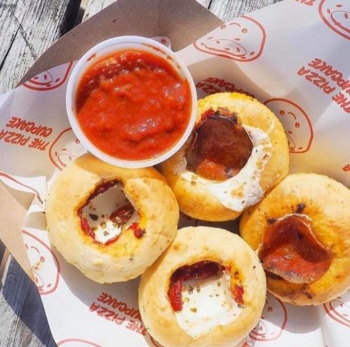 A tray of pizza cupcakes with a side of marinara sauce for dipping.