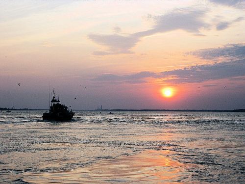 A silhouette of a boat on water at sunset, with vibrant orange and purple hues in the sky and reflections on the surface.