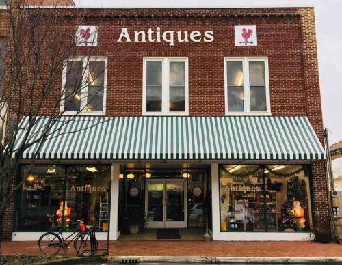A brick building with a striped awning, labeled "Antiques," featuring large windows and a bicycle parked outside.