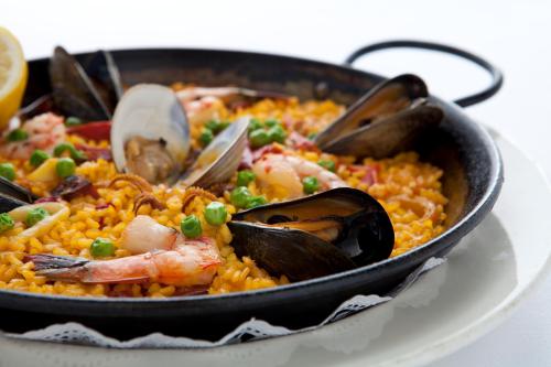 A close-up of a seafood paella with shrimp, mussels, clams, and green peas, garnished with lemon slices.