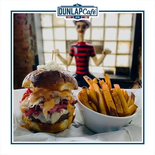 A delicious burger with toppings and fries, set against a backdrop featuring a mannequin in a striped shirt.