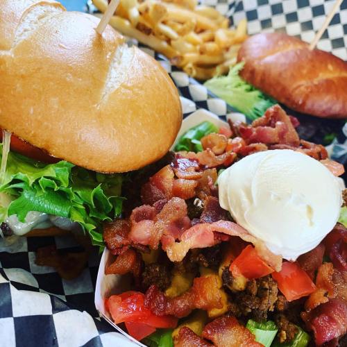 Two burgers with lettuce and tomato, accompanied by a bowl of bacon, ground meat, and diced tomatoes, plus fries.