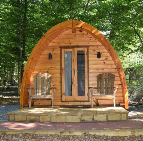 A cozy wooden cabin with an arched roof, two chairs on a porch, surrounded by trees.