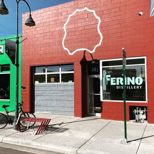 Exterior of Ferino Distillery, featuring a red brick facade, large windows, and a bicycle parked outside.