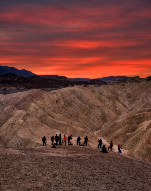 Photographers silhouetted against a vibrant sunset in a rugged desert landscape.