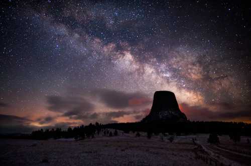 A stunning night sky filled with stars and the Milky Way above a silhouette of a prominent rock formation.