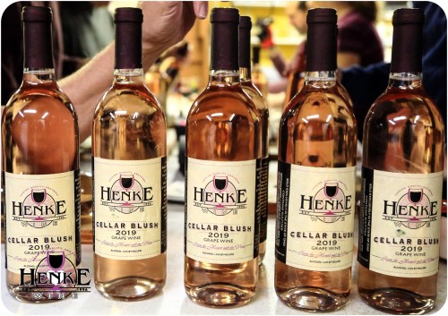 Six bottles of Henke Cellar Blush 2019 grape wine lined up on a table, showcasing their labels.
