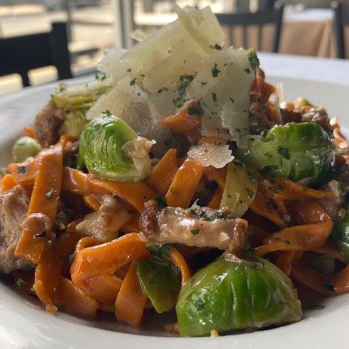 A plate of pasta with Brussels sprouts, topped with shaved cheese and herbs, served in a restaurant setting.