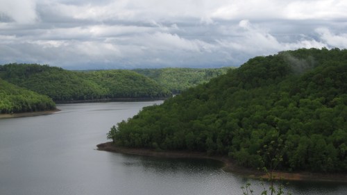 A serene lake surrounded by lush green hills under a cloudy sky.