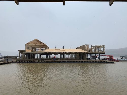 Construction of a wooden structure on a lake, with workers and snow falling in the background.