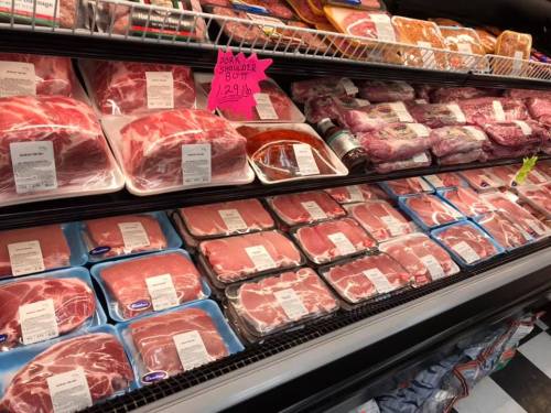 A refrigerated display case filled with various packaged cuts of meat, including pork and beef, with price tags visible.