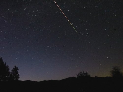 A starry night sky with a bright meteor streaking across, silhouetted mountains in the foreground.