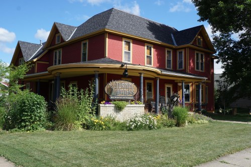 A red and yellow Victorian-style house with a sign reading "Turning Pages" surrounded by greenery and flowers.