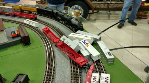 A model train setup featuring various freight cars and a steam locomotive on curved tracks.
