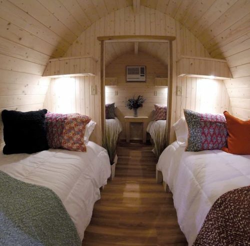 Cozy wooden interior of a cabin with two twin beds, decorative pillows, and a small table with flowers.