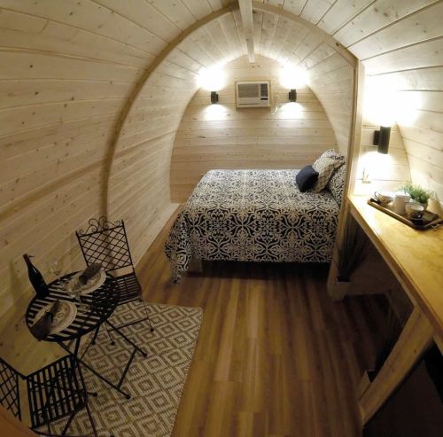 Cozy wooden interior of a small cabin with a bed, dining table, and air conditioning. Warm, inviting atmosphere.