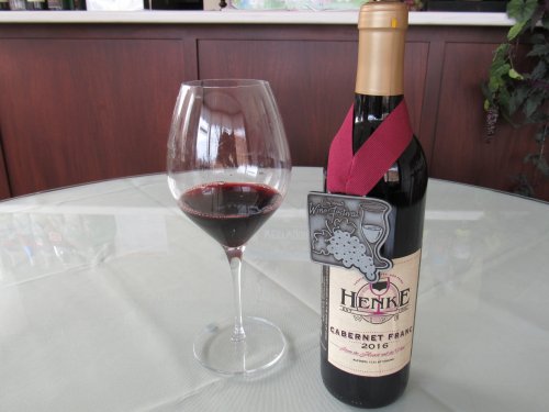 A bottle of 2016 Cabernet Franc with a medal, next to a filled wine glass on a table.
