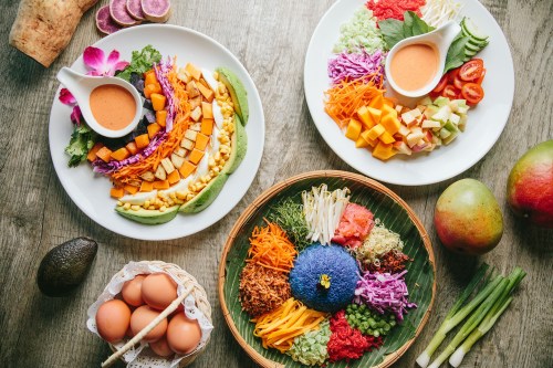 Colorful platters of fresh vegetables, fruits, and sauces arranged artistically on a wooden table.