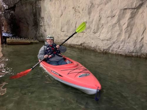 A person in a pink kayak paddles in calm water inside a cave with rocky walls.