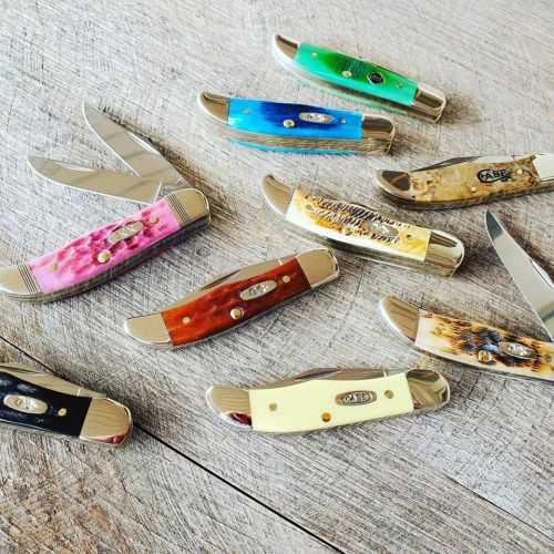 A collection of colorful pocket knives arranged on a wooden surface, showcasing various handle designs and blade styles.