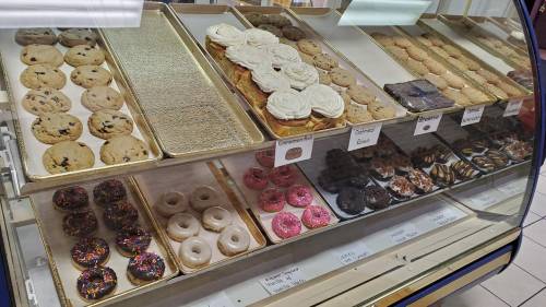 A display case filled with various cookies and donuts, including chocolate chip, frosted, and sprinkled varieties.