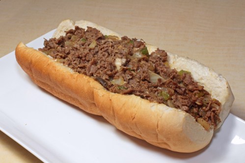 A close-up of a loaded sandwich with seasoned beef, onions, and green peppers in a soft hoagie roll.