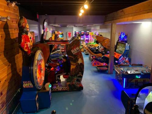 A vibrant arcade with various games, including racing and shooting, and a player engaged at a large game machine.
