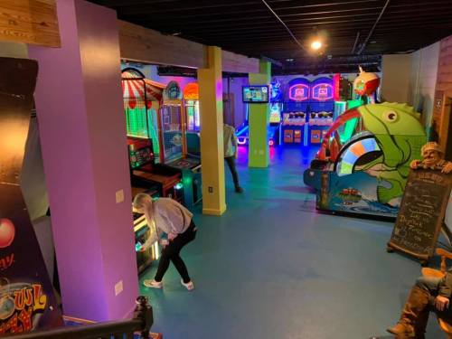 A colorful arcade with various games, including basketball and fishing-themed machines, and a person playing a game.