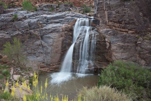 A serene waterfall cascading over rocky cliffs into a calm pool, surrounded by lush greenery.