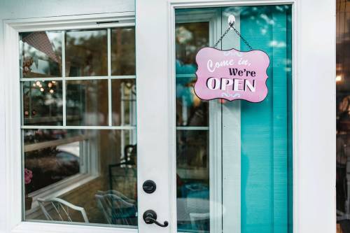 A door with a pink "Come in, We're OPEN" sign, inviting customers inside a shop.