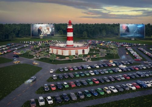 A lighthouse surrounded by a large parking lot, featuring outdoor movie screens and cars parked in rows.