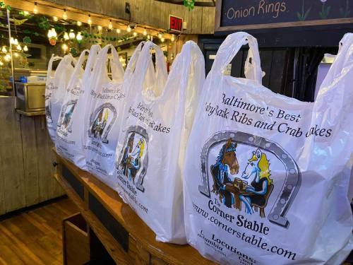 A row of takeout bags with "Baltimore's Best" branding on a wooden counter, decorated with string lights.