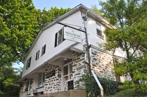 Historic building with a stone facade, featuring a sign for the Appalachian Trail Visitor Center and surrounded by greenery.