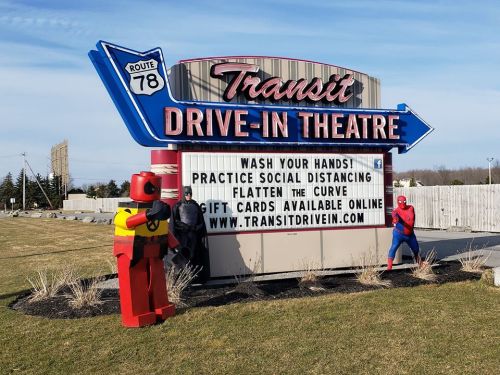 A drive-in theater sign displays health messages, with a robot and Spider-Man posing nearby.