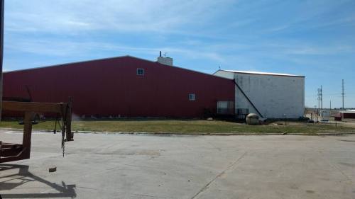 A large red barn-like building with a white section, set against a clear blue sky and grassy area in the foreground.