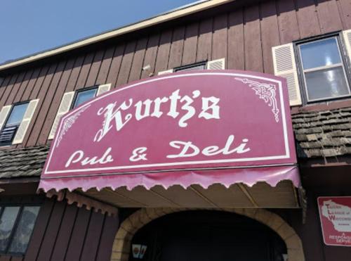 Sign for "Kurtz's Pub & Deli" on a building with a purple background and decorative lettering.