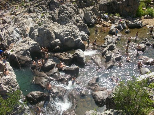 Aerial view of a natural swimming area with people enjoying the water among large rocks and greenery.