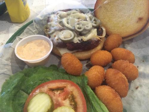 A burger with jalapeños and cheese, served with a side of hushpuppies, lettuce, tomato, and pickles.