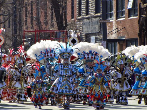 A vibrant parade featuring performers in colorful, feathered costumes marching down a city street.