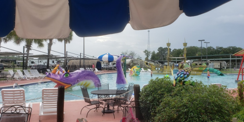 A colorful pool area with whimsical decorations, including large fish and birds, under a blue canopy.