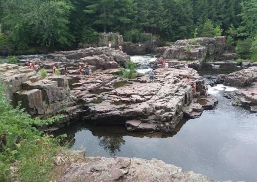 People exploring rocky terrain near a river, surrounded by lush greenery and small waterfalls.