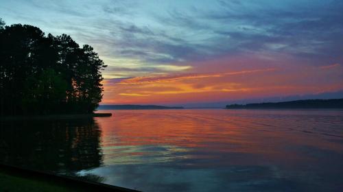 A serene lake at sunset, reflecting vibrant colors in the water, surrounded by trees and a calm sky.