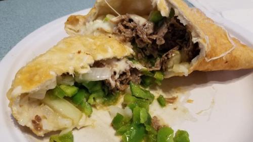 A close-up of a stuffed fried pastry filled with beef, onions, and green peppers on a white plate.